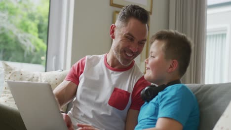 feliz padre caucásico con su hijo sentado en la sala de estar y usando una computadora portátil