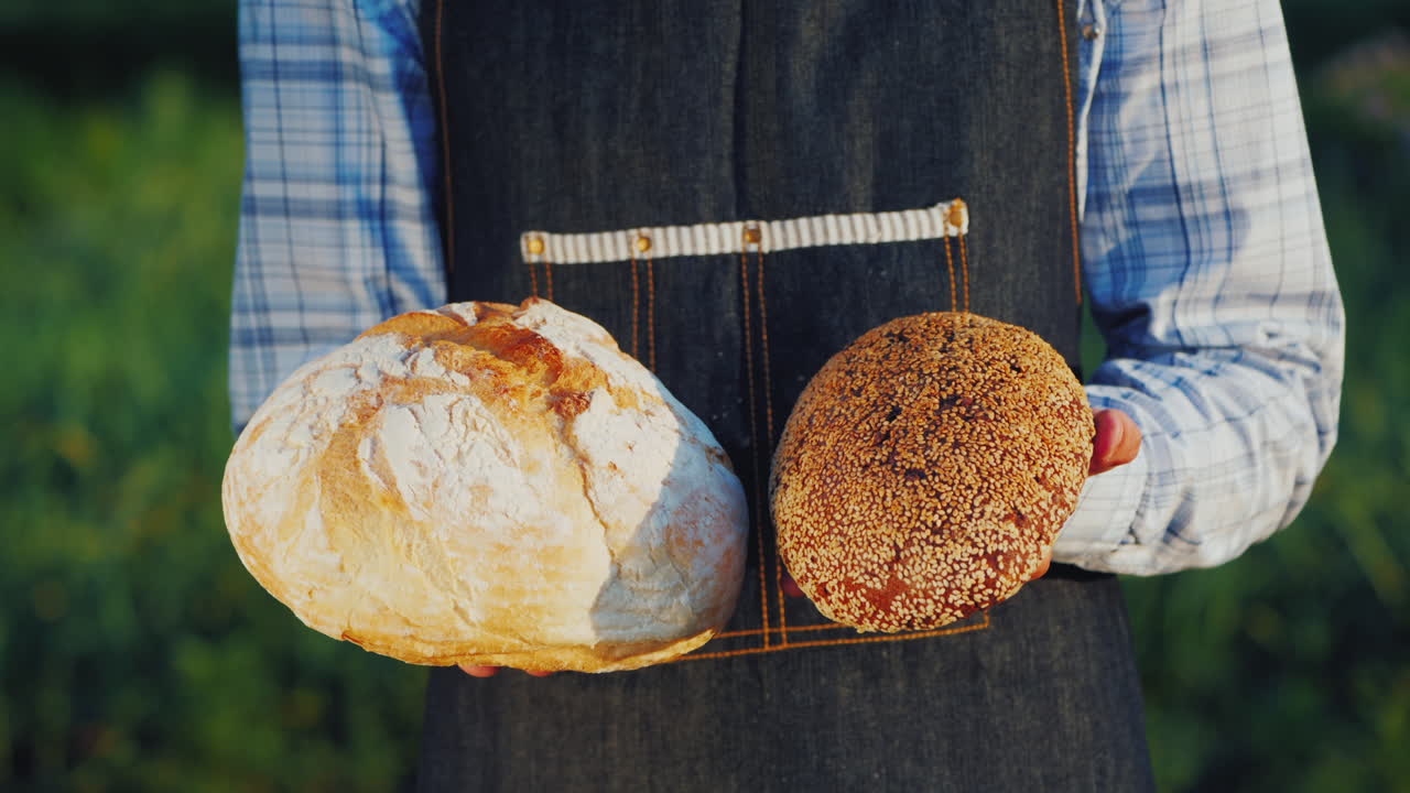 un panadero sostiene dos hogazas de pan claro y oscuro