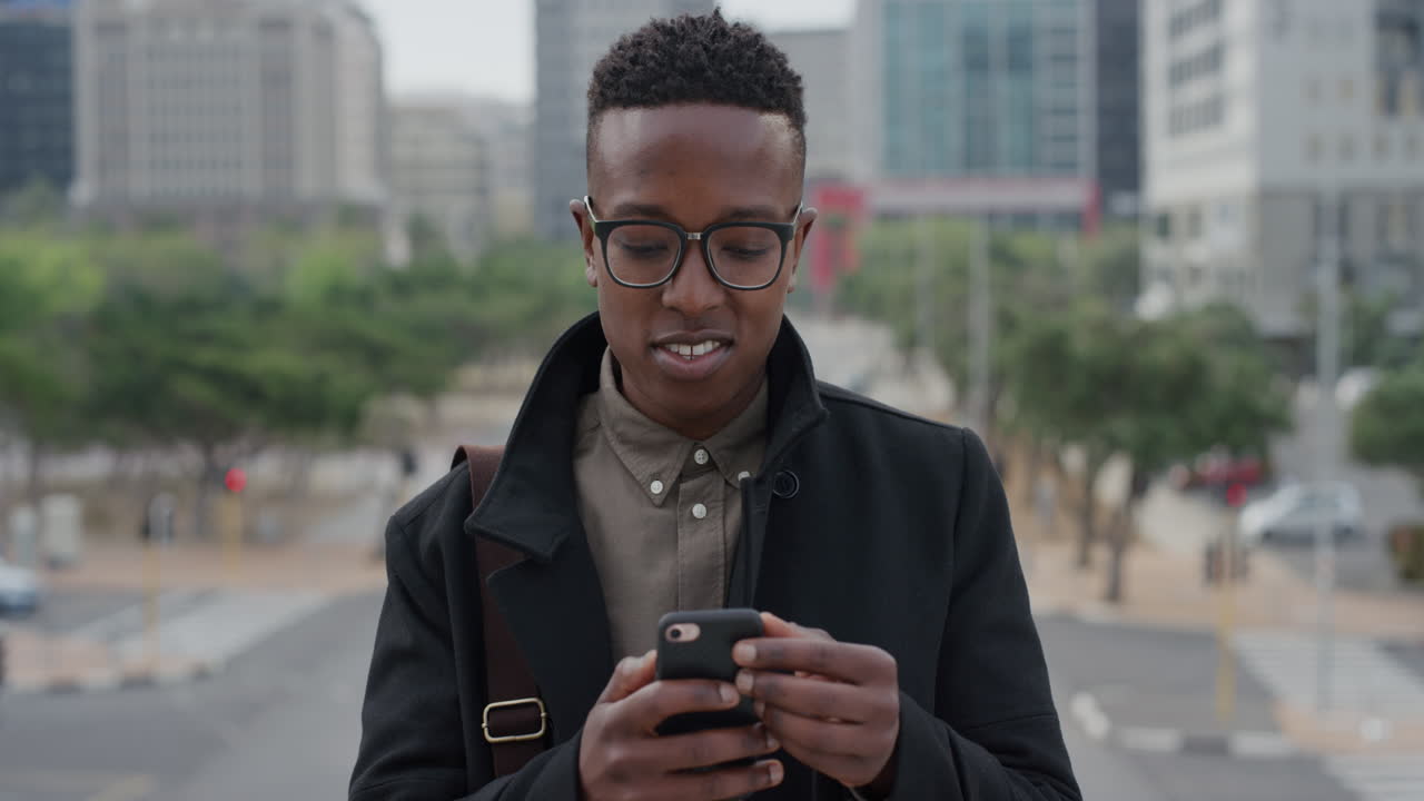 portrait young african american man student using smartphone in city texting browsing messages on mobile phone looking around enjoying urban lifestyle slow motion
