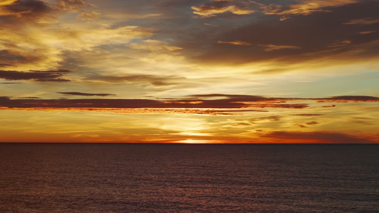 Ocean horizon at sunset with vibrant orange and gold clouds reflecting light