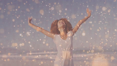 woman raising arms at beach edge, with soft golden light particles highlighting wellness concept
