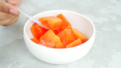 close-up of a person eating cubed papaya from a white bowl