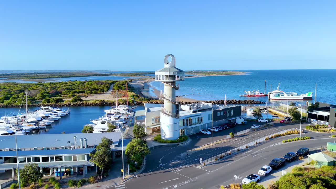 Aerial footage of Queenscliff Marina with lighthouse, boats, and coastline under clear blue skies