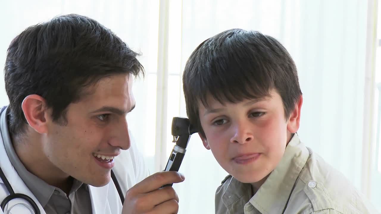 близкий снимок врача, осматривающего уши маленьких мальчиков.
