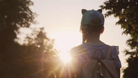 Un-Niño-Con-Una-Mochila-Está-De-Pie-En-El-Parque,-La-Atardecer-Brilla-Sobre-él