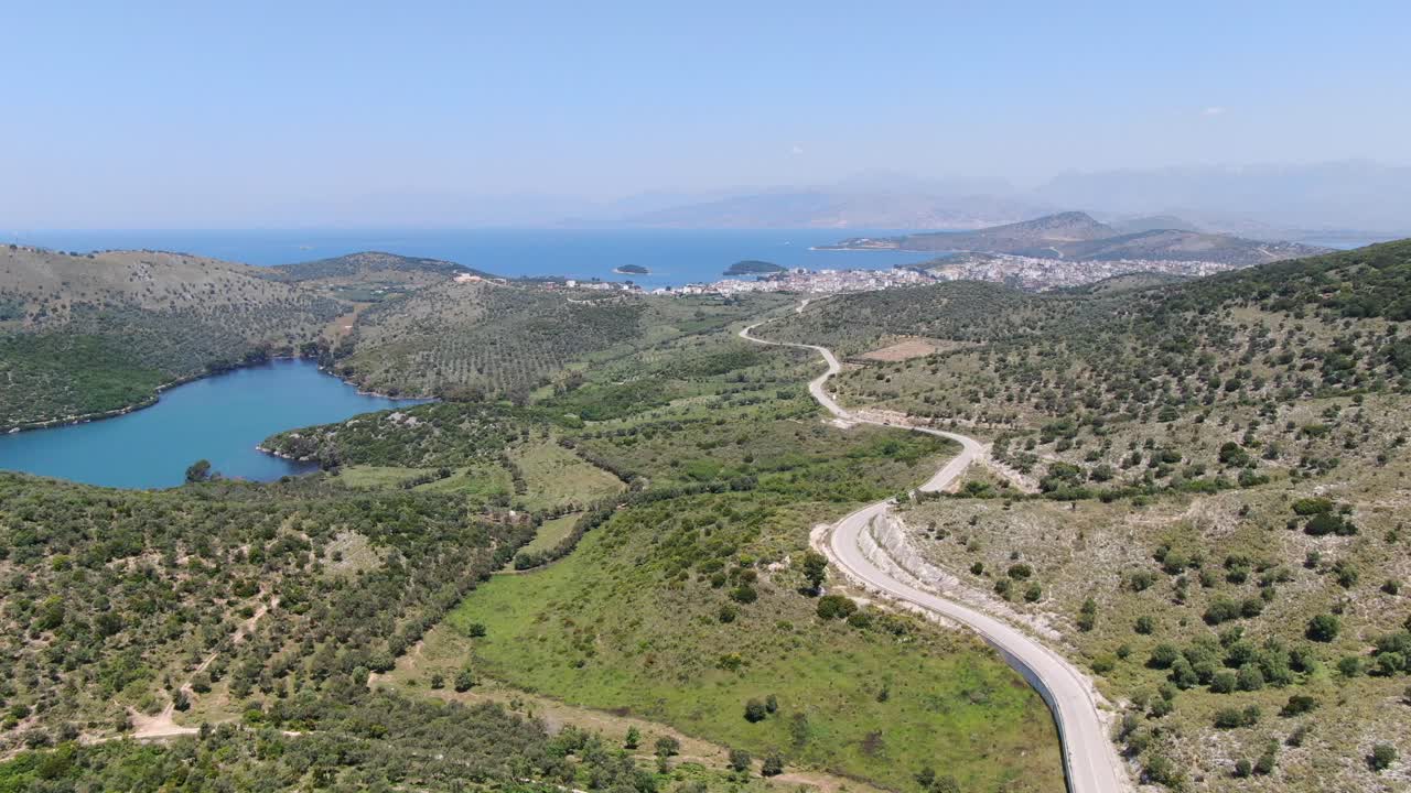 vista de avión no tripulado en albania volando sobre un amplio río, una carretera curva y un paisaje verde junto al mar con montañas en la parte de atrás