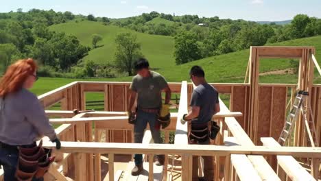 three workers are constructing a wooden frame structure on a bright day. the crew is engaged in various activities as they prepare the building site surrounded by lush greenery.