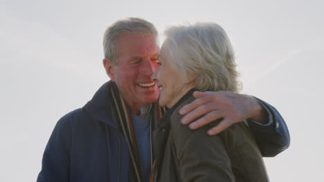 Loving-Active-Senior-Couple-Hugging-As-They-Stand-Outdoors-Against-Flaring-Sun