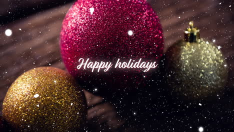 animation of happy holidays text and snow falling over christmas baubles