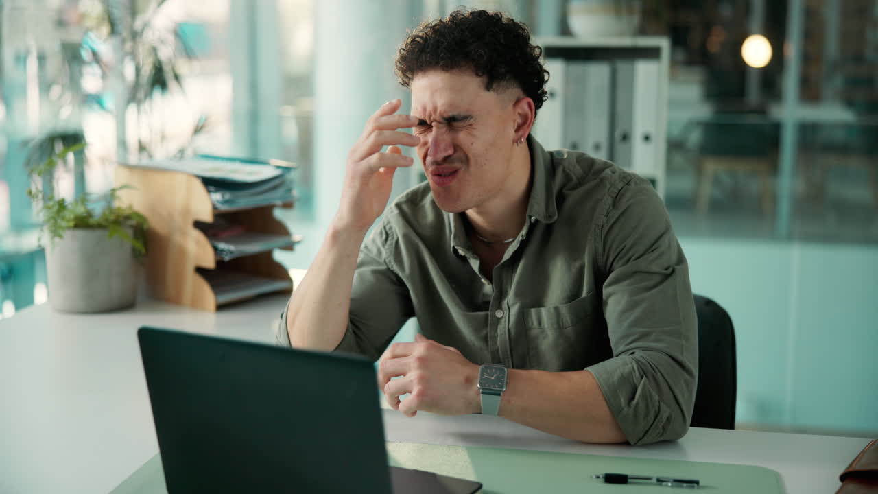 Frustrated Young Man Experiencing Headache While Working on Laptop in Office