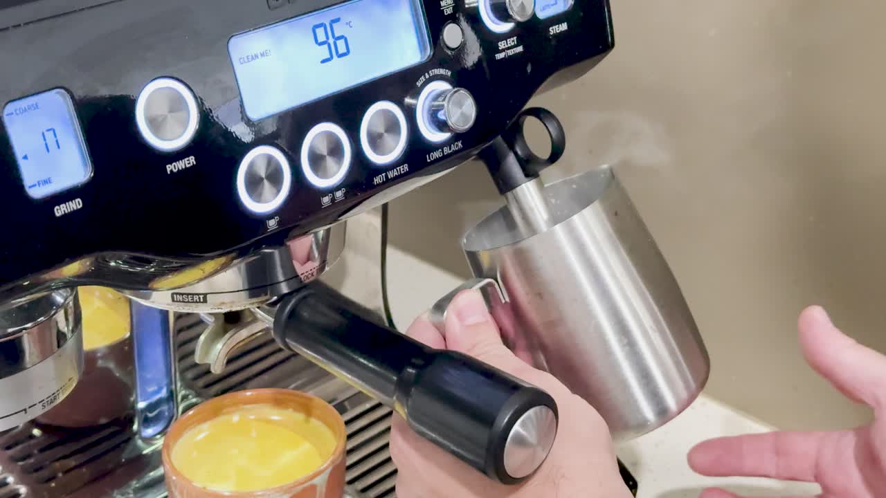 Hands frothing milk using an espresso machine steam wand in a well-lit kitchen setting