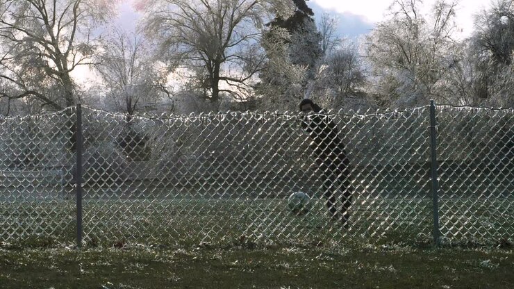 SLOW MOTION: A man kicks a soccer ball into an icy fence which explodes the shattered ice into the air