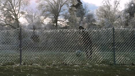 slow motion: a man kicks a soccer ball into an icy fence which explodes the shattered ice into the air