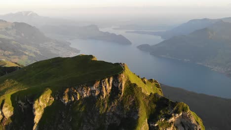 aerial flyover over the summit of niederbauen chulm with a view of lake lucerne, burgenstock and pilatus in the background on a golden summer morning in the swiss alps