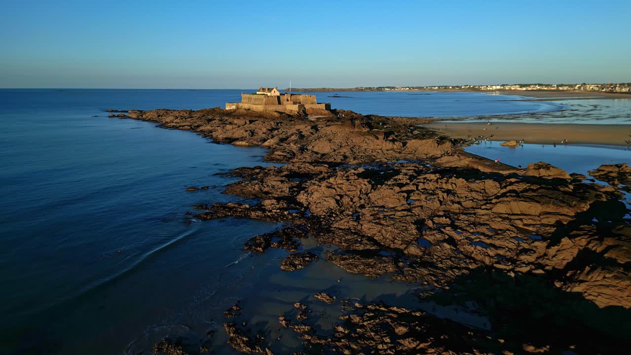 Fort National tidal island during shallow water at sunset on sideways drone movement, Saint-Malo, France.