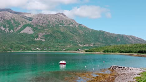 Barco-Flotando-En-Las-Aguas-Cristalinas-Del-Mar-Con-El-Pico-De-La-Montaña-Lonketinden-Al-Fondo-En-La-Isla-Senja,-Noruega