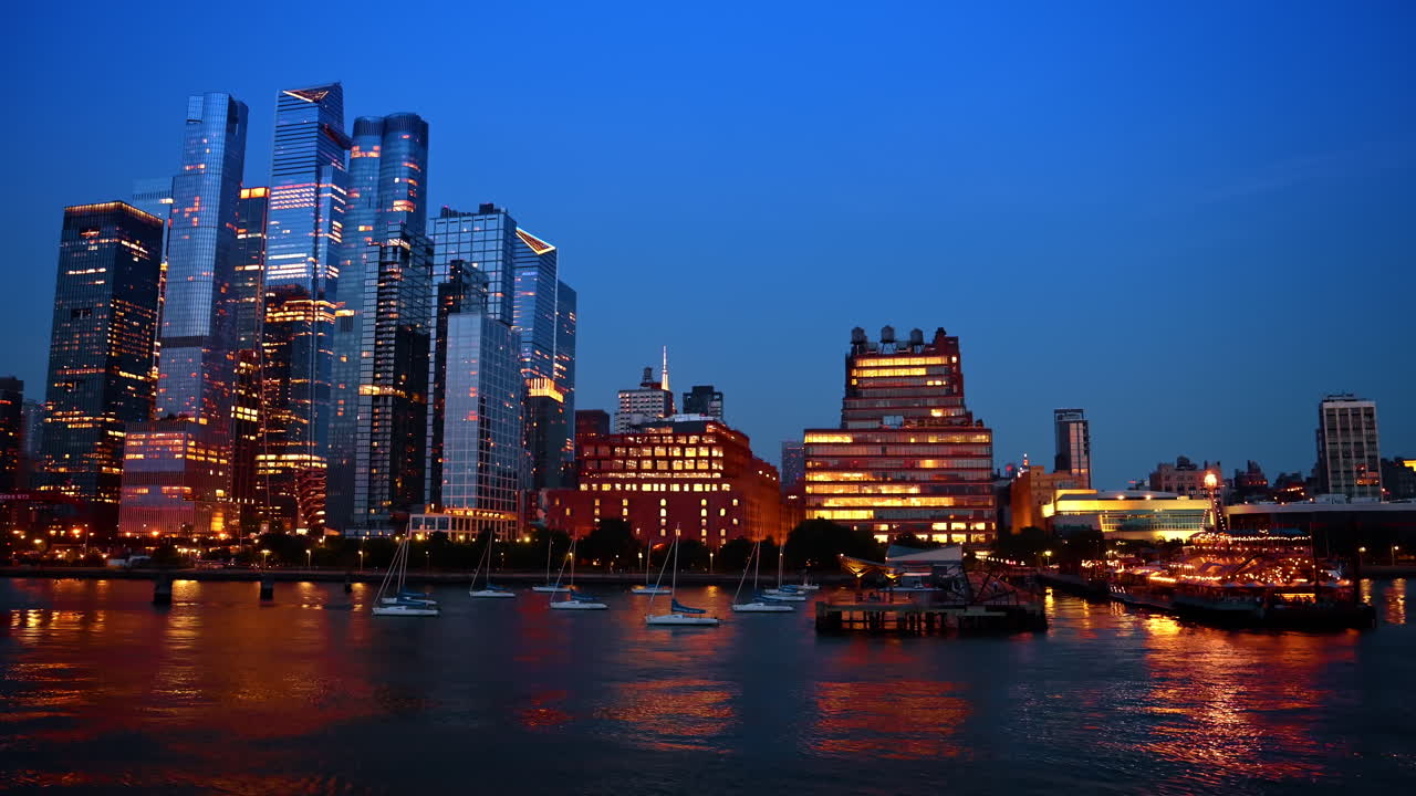 New York, Hoa Kỳ, ngày 25 tháng 5 năm 2025: Các tòa nhà chọc trời ở West Side Manhattan và thuyền buồm trên sông vào ban đêm. Quang cảnh kiến trúc Hudson Yards và thuyền buồm neo đậu trên sông Hudson ở thành phố New York vào buổi tối.