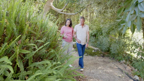 senior diverse couple enjoying nature walk, admiring trees and plants in lush garden
