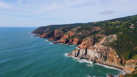 rough coastal rocky slopes meeting deep blue ocean aerial view. waves rolling