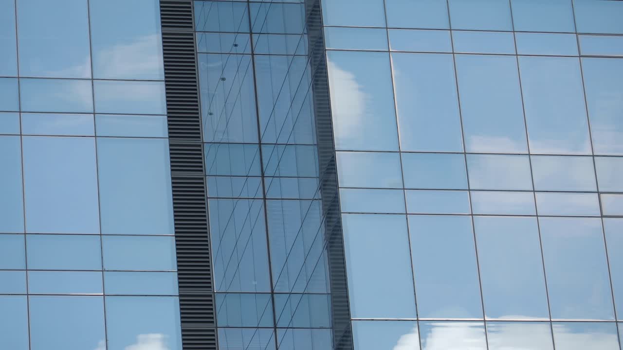 Vista de um edifício moderno de vidro com o céu azul refletido nas janelas.