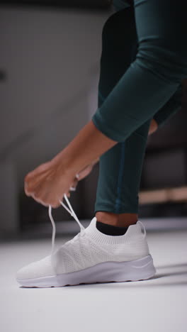 vertical video close up of female athlete in gym or changing room tying laces of training shoe before exercising 1