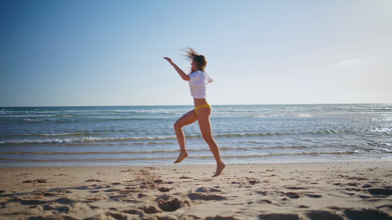 Ragazza felice che gioisce delle onde del mare in una giornata estiva e soleggiata. Donna in vacanza che corre sulla spiaggia