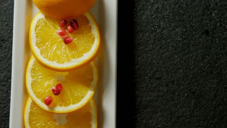 Slice-of-orange-with-pomegranate-seeds-in-tray-on-black-background-4K-4k