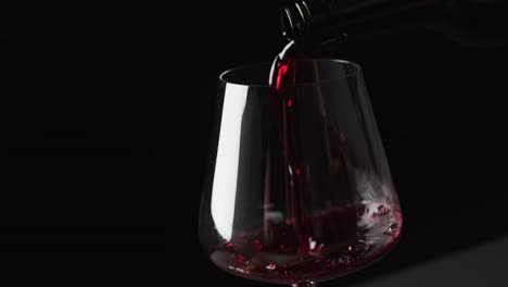 red wine pouring into glass on black background with copy space