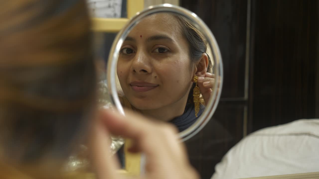 Giovane e bella donna asiatica che si guarda allo specchio indossando orecchini d'oro 18k certificati HUID.