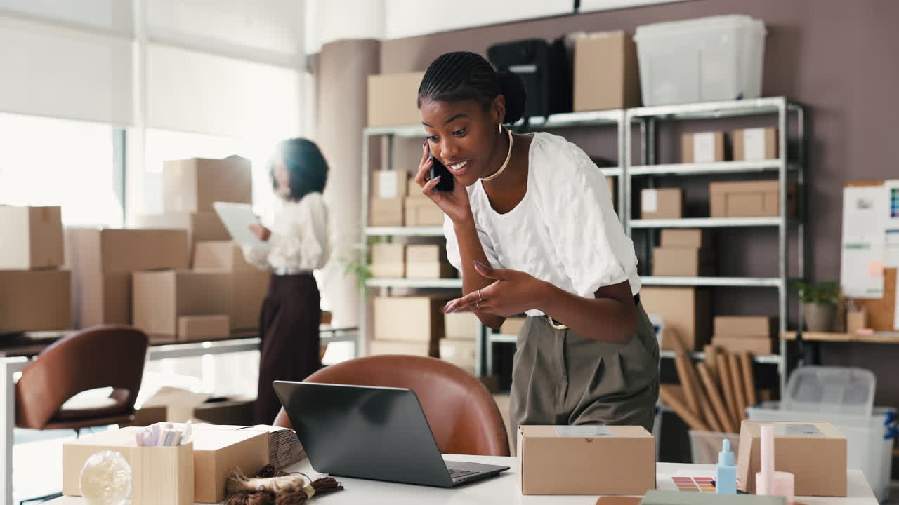Giovane donna che parla al telefono e usa il laptop in un ufficio e-commerce.