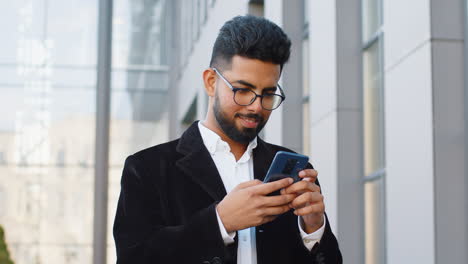 Lächelnder-Geschäftsmann,-Der-Sein-Smartphone-Benutzt-Und-Textnachrichten-Eintippt-Und-Auf-Der-Stadtstraße-Online-Chattet