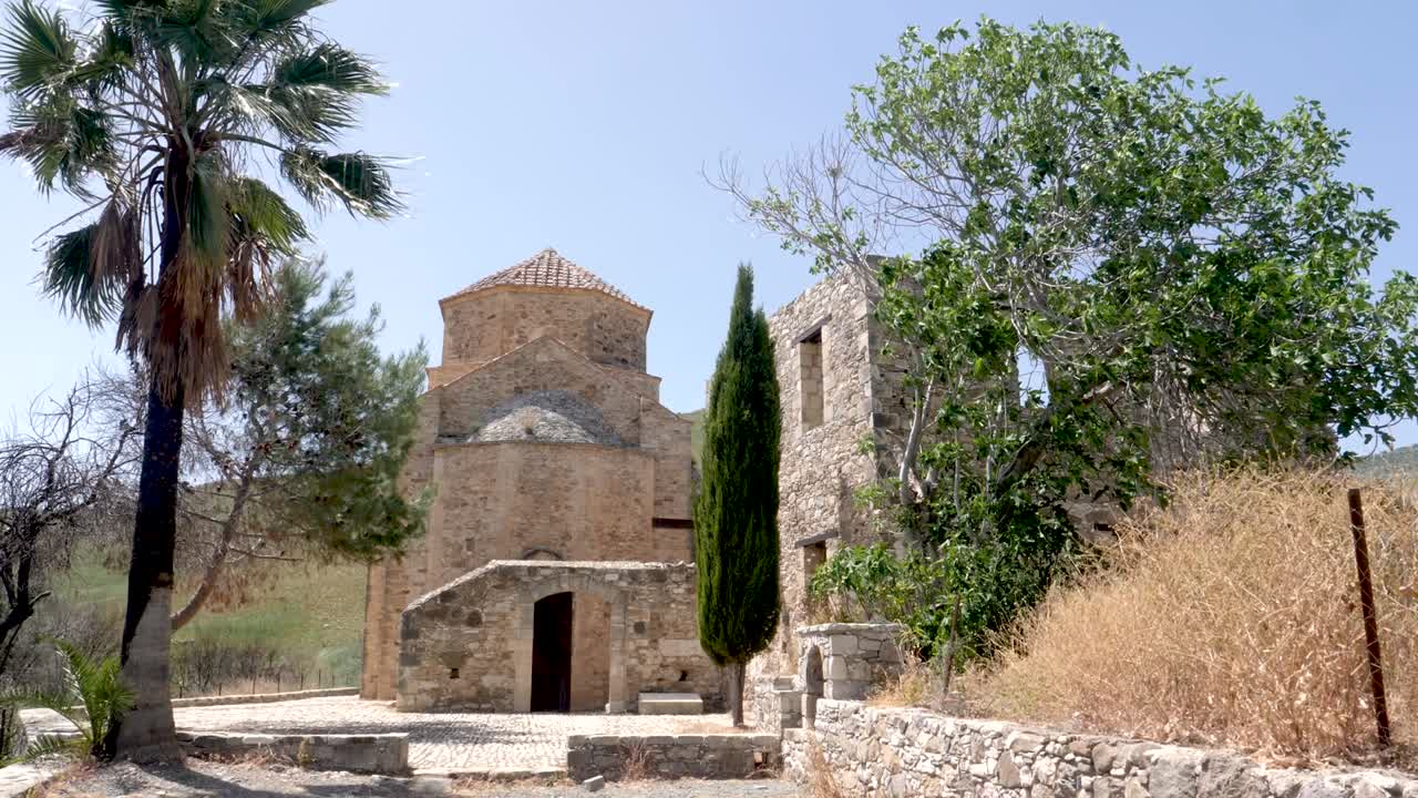 Una chiesa di pietra abbandonata si erge tra alberi alti ed erba secca in una serena località rurale. La struttura mette in mostra un'architettura complessa e un'atmosfera tranquilla, perfetta da esplorare.