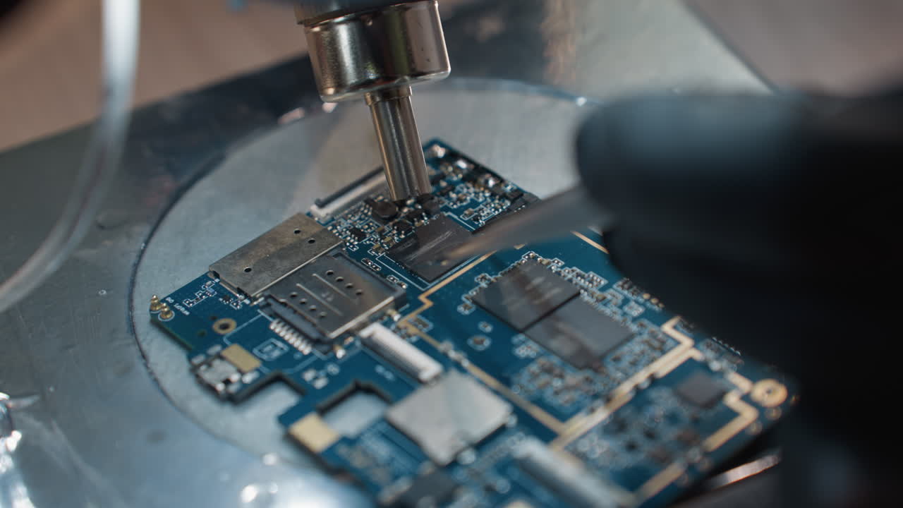 A close-up view of a technician's gloved hands using a precision tool and a soldering iron to work on a circuit board under a microscope