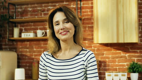 Portrait-Of-The-Young-Beautiful-Woman-With-Fair-Hair-Standing-At-The-Kitchen-And-Looking-To-The-Camera-With-A-Smile