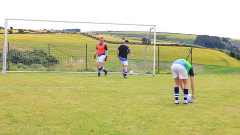 Male soccer players playing soccer, practicing shooting at goal with goalkeeper on pitch, copy space