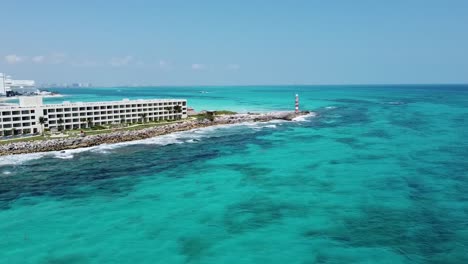 cancun coastline with lighthouse and hotel, clear blue waters under sunny skies, aerial view