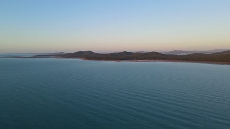 calm waters of ocean with clairview town in the distance at dusk - seascape of isaac region in queensland, australia