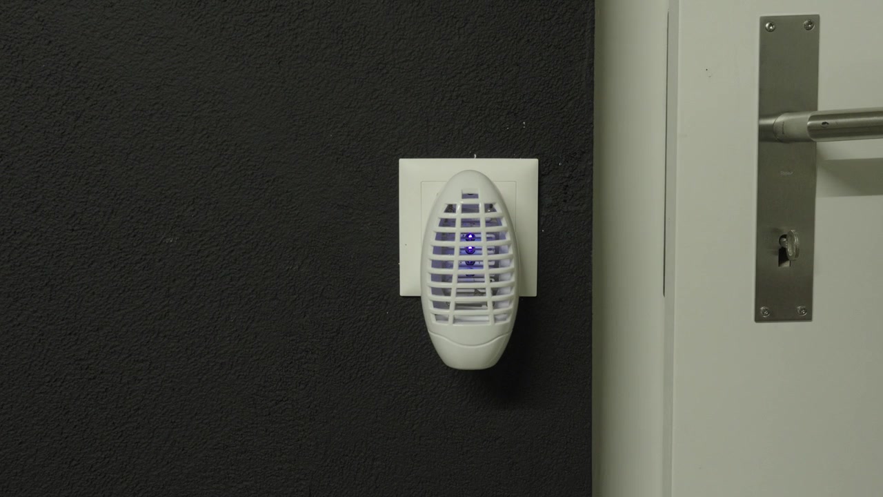 Una mano inserisce un dispositivo elettrico antizanzare in una presa a muro prima che si illumini di blu in una stanza buia
