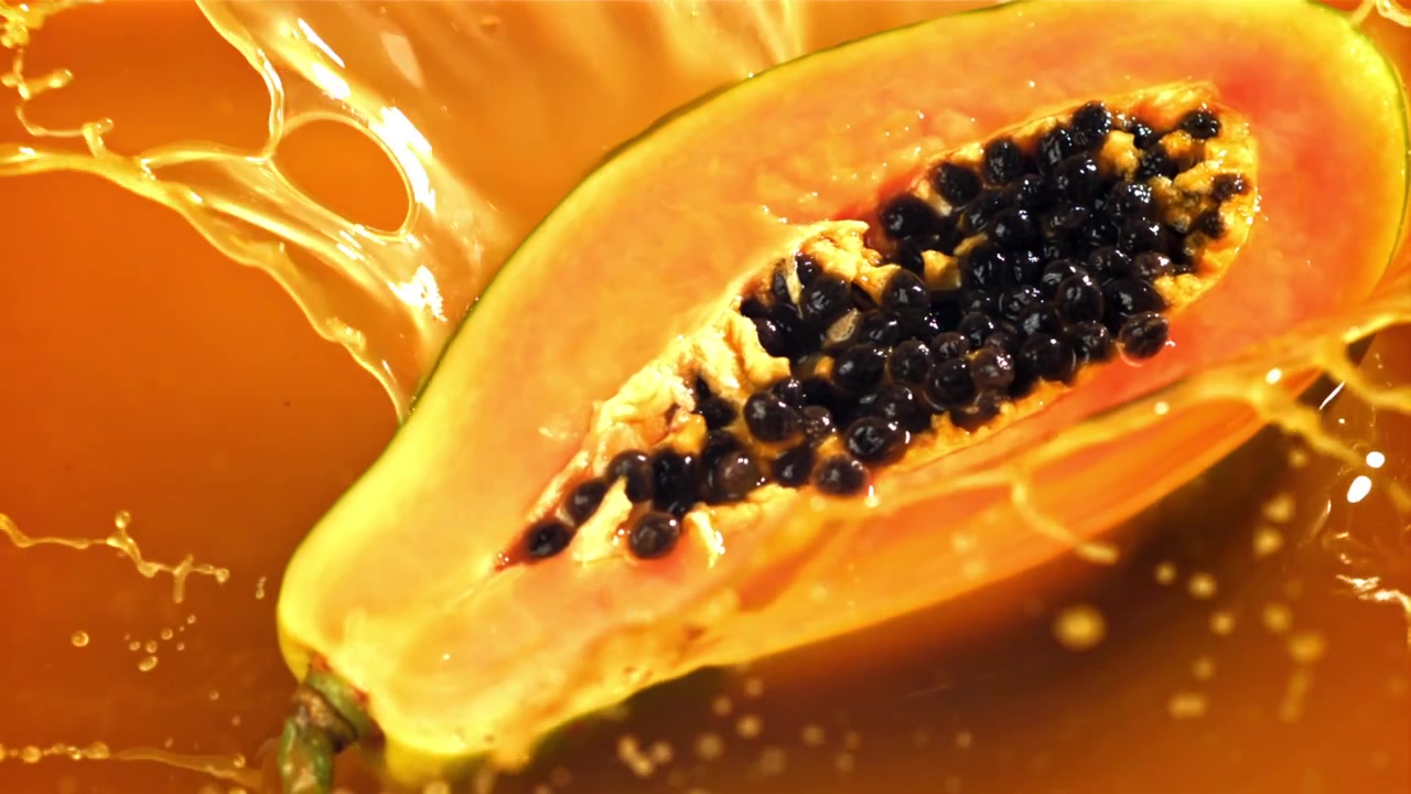 Frisk papaya-halvdel plasker ned i livlig oransje væske