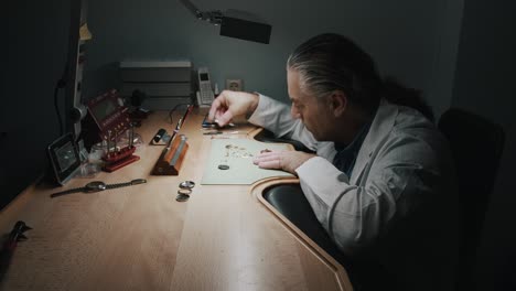 A-watchmaker-carefully-removing-the-parts-of-a-wristwatch-he's-repairing---wide-shot