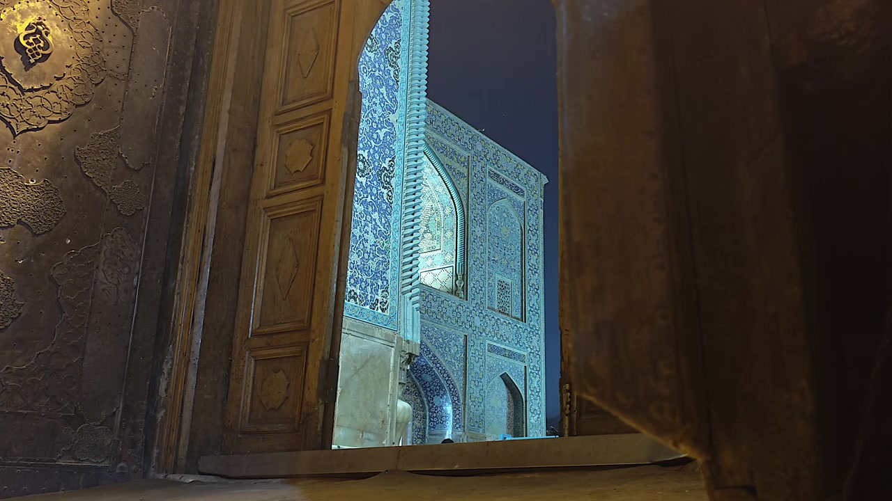 Person Walking Through Ornate Wooden Doorway of Historic Mosque at Night