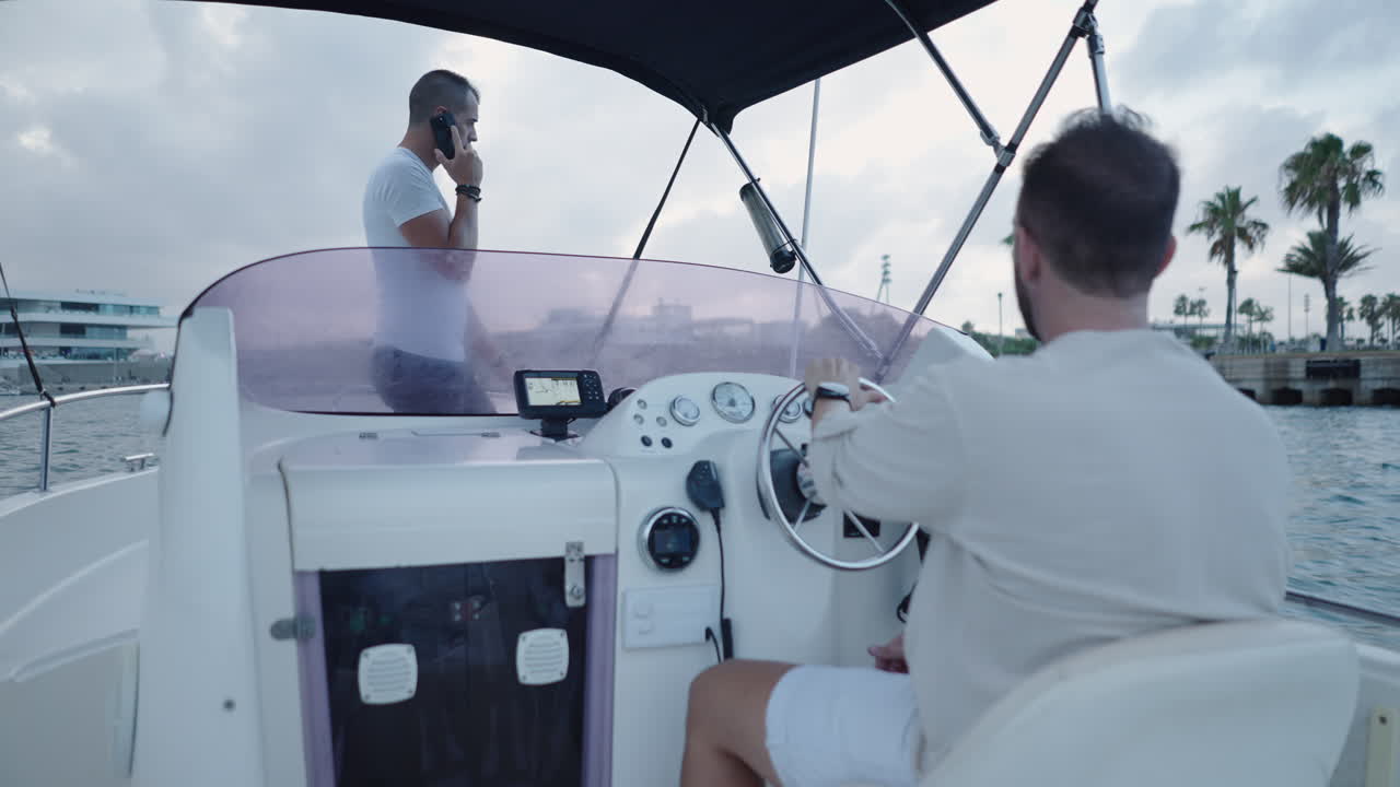 Two Men on a Boat, One Driving and Another Talking on the Phone