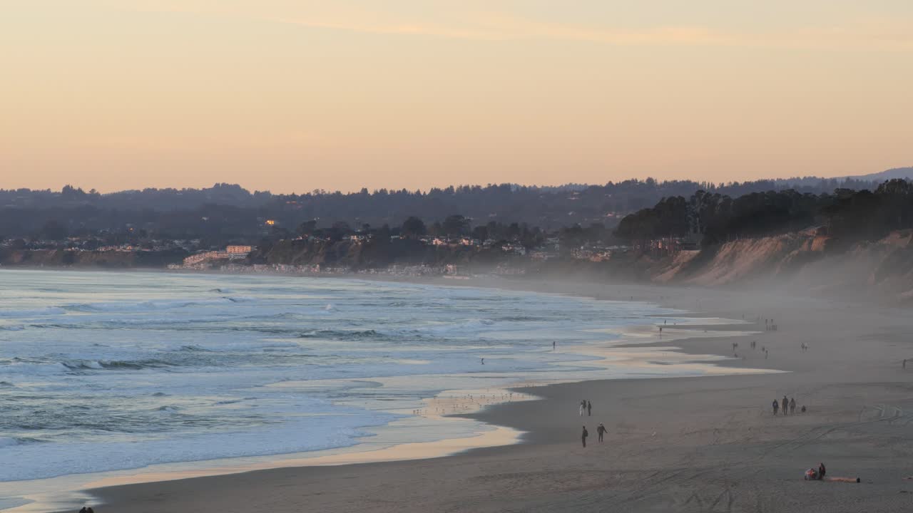 Santa Cruz beach during sunset golden hour. People walking on beach