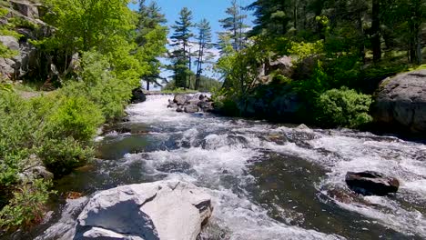 fast rushing water flows around boulders in river rapids in slow motion, wide pedestal up