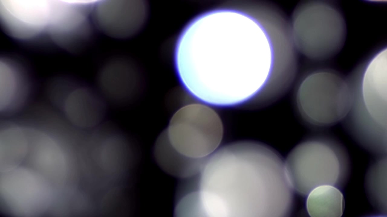 Luci bokeh bianche fluttuanti con riflesso lente su sfondo scuro