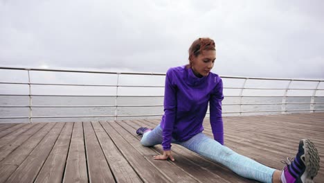 Athletic-woman-stretching-her-legs-before-a-jog-on-the-beach-by-the-sea-early-in-the-morning.-Young-girl-doing-splits.-Training