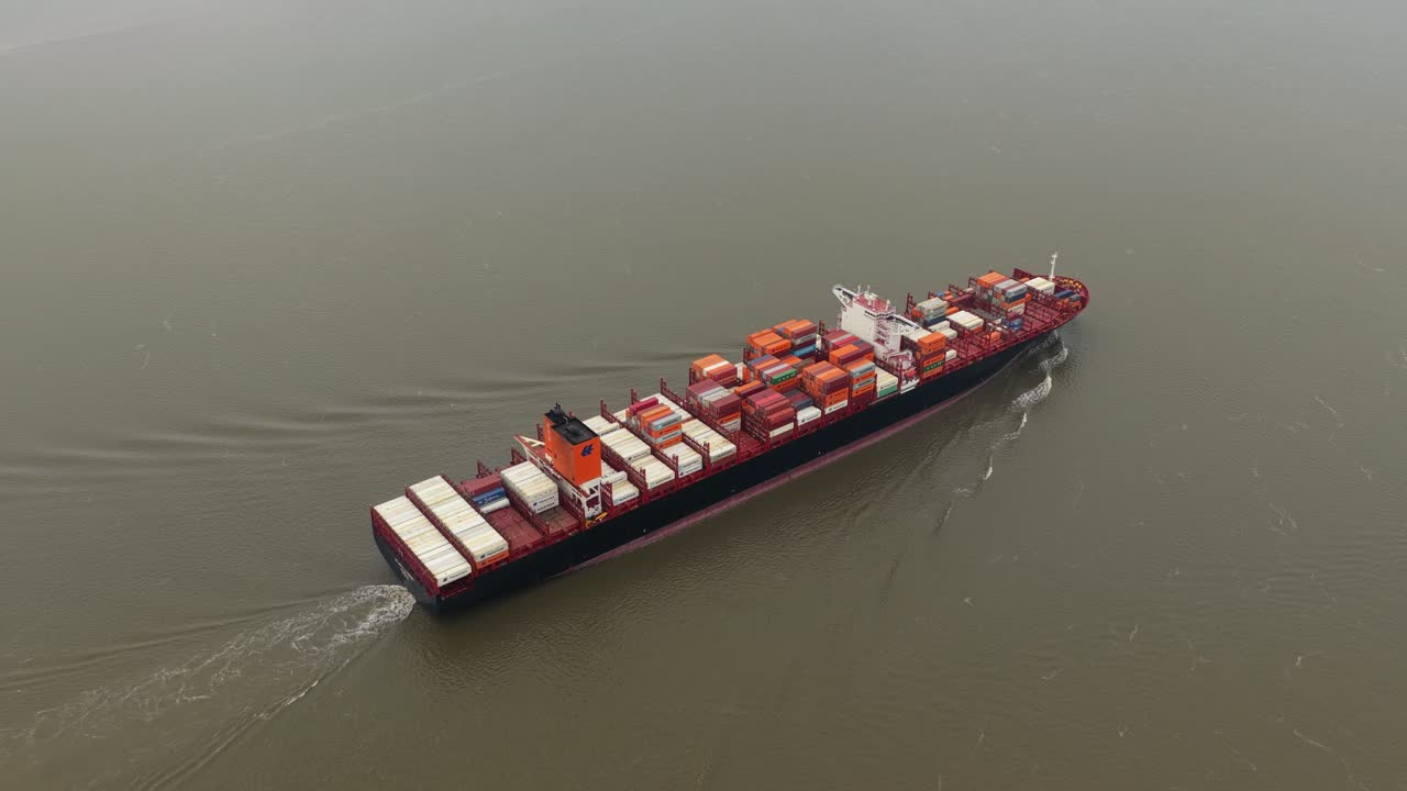 Drone view of shipping vessel heading to ocean from port facility