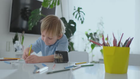 The-boy-sitting-at-the-table-in-the-living-room-writes-a-letter-to-his-father-and-draws-a-picture-of-the-family-with-a-pencil