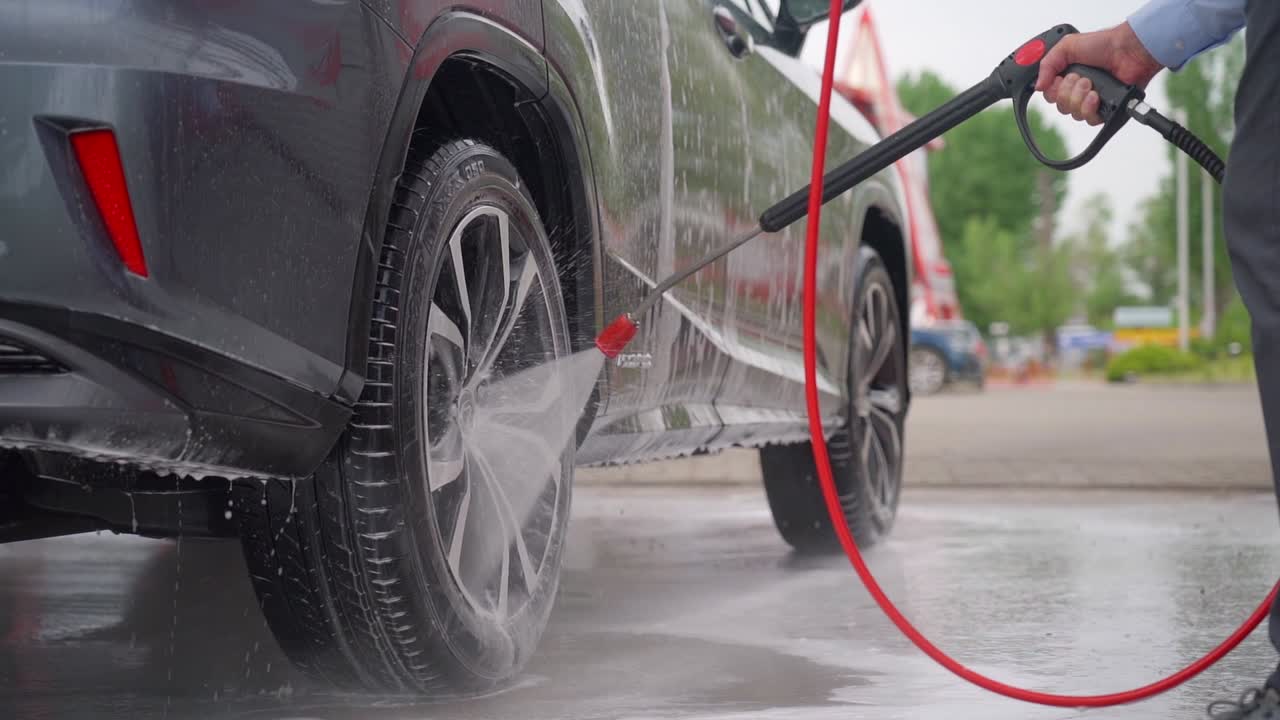 Pessoa usando uma lavadora de alta pressão para limpar rodas de carro em um lava-rápido manual.