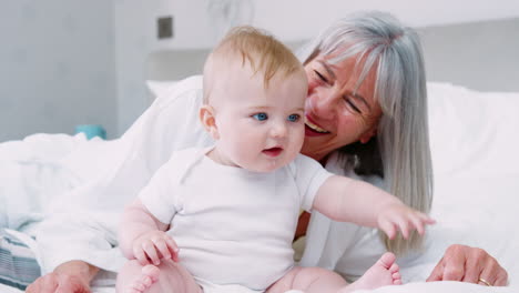 grandmother lying in bed at home looking after baby grandson